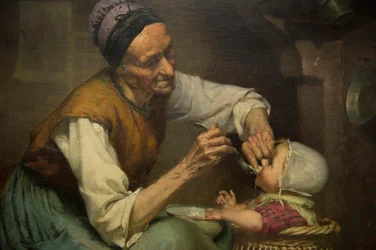 Una vecchia donna nutre la sua nipotina tenuta in un girello di vimini