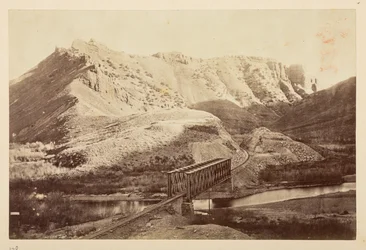 Vedute sulla ferrovia del Pacifico, binario ferroviario che attraversa un fiume su un ponte a travi, con montagne sullo sfondo