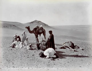 Cammellieri egiziani durante una pausa nel deserto. In primo piano, due membri del piccolo gruppo sembrano pregare