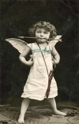 Bambino piccolo, vestito da Cupido, con una freccia in bocca