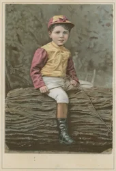 Bambino in abiti da fantino seduto su un tronco
