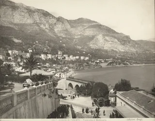 Vista panoramica di Montecarlo a Monaco. La scena mostra vari passanti; a sinistra vediamo un primo piano di una balaustra di marmo