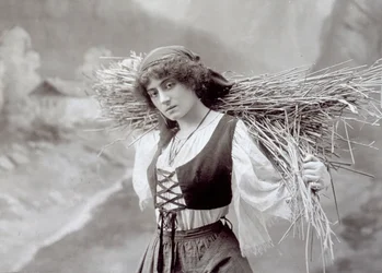 Giovane donna in abito tradizionale che porta un fascio di paglia
