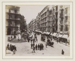Veduta di Via Roma a Napoli con una statua, negozi, carrozze a cavalli e passanti