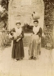 Due giovani donne che indossano abiti tradizionali e trasportano giare di terracotta vicino a un pozzo, Marche, Italia, 1910 ca.