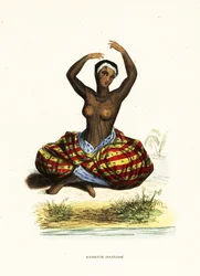 Giovane donna tatuata e a seno nudo che danza una hula seduta a terra