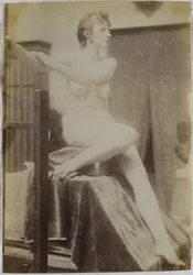 Studio di un modello femminile nudo, seduto su un podio accanto a un cavalletto e visto di fronte, nell
