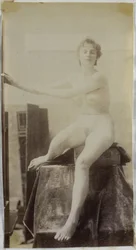Studio di un modello femminile nudo, seduto su un podio accanto a un cavalletto e visto di fronte, nell
