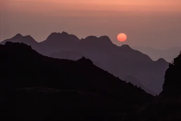 Un sole brillante color cremisi e arancione tramonta sulla catena montuosa di Yan Shan