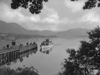 Una barca che trasporta persone su un lago si avvicina a un pontile, sullo sfondo le montagne