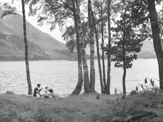 Una famiglia che si rilassa vicino al lago con gli alberi a destra e le montagne sullo sfondo