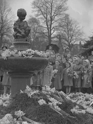 Bambini che depositano mazzi di narcisi sulla fontana con statua in alto