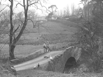 Due ragazze sedute su un ponte di pietra sul fiume Cocker ai piedi di Scale Hill, mentre osservano le oche nella stradina a Loweswater