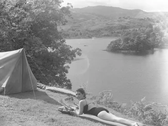 Veduta di una giovane donna in costume da bagno e sdraiata su un lilo, sullo sfondo un lago