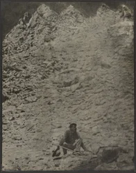 [Uomo accovacciato in un paesaggio roccioso]
