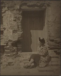 [Donna seduta davanti a un edificio in rovina]