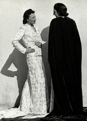 Due modelle presentano creazioni della casa di moda italiana "Dragoni". Una modella indossa un abito in tessuto operato composto da giacca e lunga gonna con strascico. L