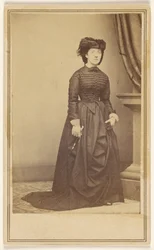 [Donna non identificata con cappello e lungo abito scuro.]