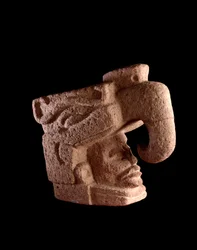 Arte precolombiana, civiltà maya, periodo preclassico: scultura in pietra raffigurante la testa di un uomo che emerge dalla bocca di un dio zoomorfo simile all