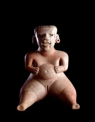 Arte precolombiana, civiltà maya, periodo preclassico: statuetta in argilla raffigurante una donna seduta con il ventre gonfio e le gambe divaricate (partoriente?). Da Kaminaljuyú, Guatemala. 19 x 25 cm. Guatemala, Museo Nacional de Arqueología y Etnología