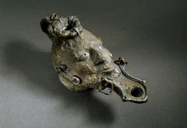 Arte romana: lampada ad olio in bronzo a forma di volto. I-II secolo d.C. Spagna, Museo di Ampurias (Empurias)