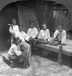 Donne birmane che fumano fuori dalla loro casa, Mandalay, Birmania, 1908