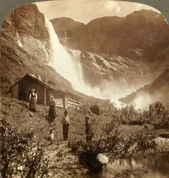 Umile casa di montagna ai piedi delle scogliere dove le cascate di Skiaeggedals saltano 525 piedi, Norvegia, c1905