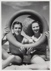 Uomo e donna che guardano attraverso un anello di gomma sulla spiaggia, c 1935