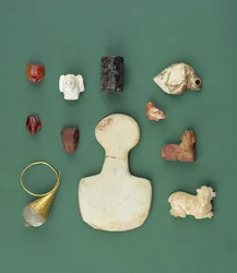 Collezione di oggetti del Mediterraneo orientale tra cui un amuleto di avvoltoio sumero, un sigillo di serpentino accadico e una rana di corniola mesopotamica, datati tra il 3300 e il 2000 a.C.