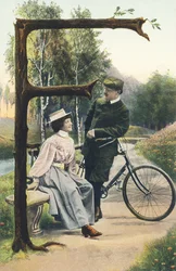 F : Un uomo in tenuta da ciclista appoggiato sulla sua bicicletta discute con una donna seduta su una panchina. Ambiente campestre - Alfabeto personaggi Rif Th. E., L. Theochrom - Serie 994. Theodor Eisman, editore, Lipsia