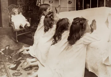 Quattro bambine inginocchiate accanto a un letto mentre recitano la preghiera serale
