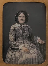 Anziana donna seduta con vestito a quadri e cappellino